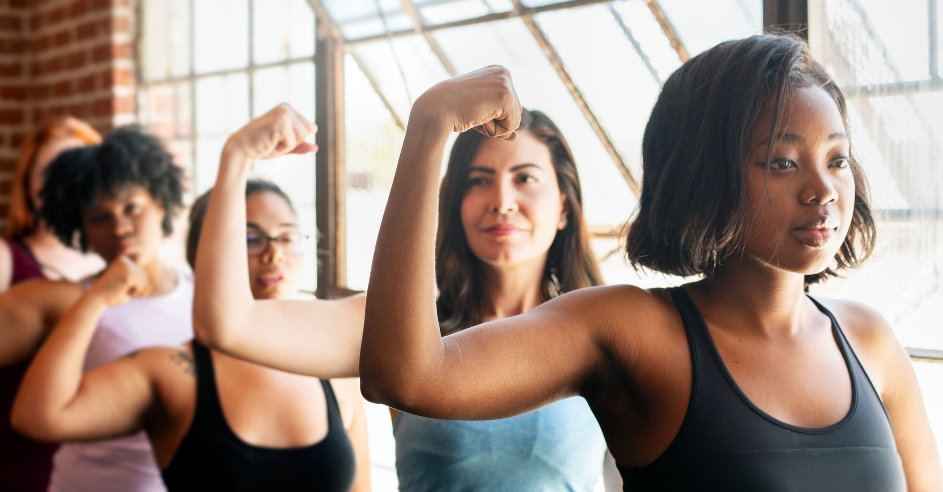 Diverse group of sportswomen flexing arms in a gym.